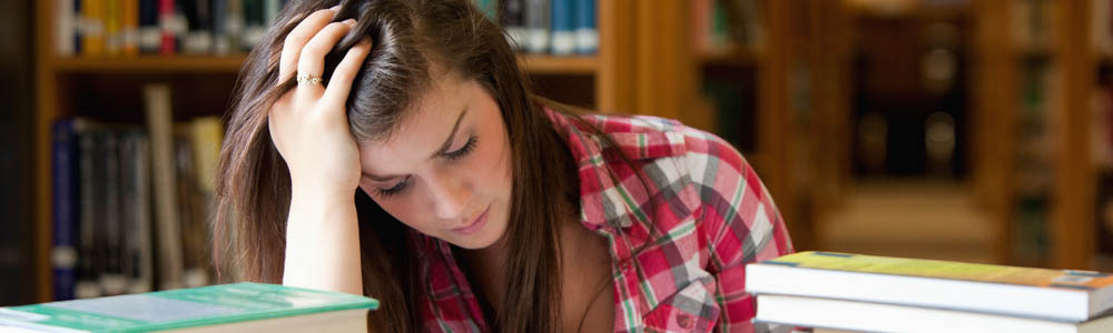 Frustrated female college student looking stressed while reading a textbook in the library Frustrated female college student looking stressed while reading a textbook in the library